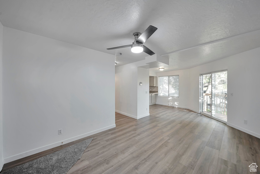 Unfurnished living room featuring ceiling fan, a textured ceiling, and light wood-type flooring
