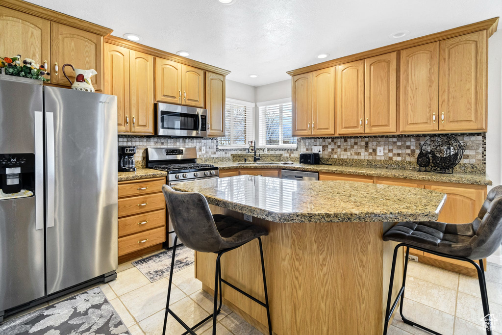 Kitchen featuring a kitchen island, appliances with stainless steel finishes, light tile patterned floors, and a kitchen bar