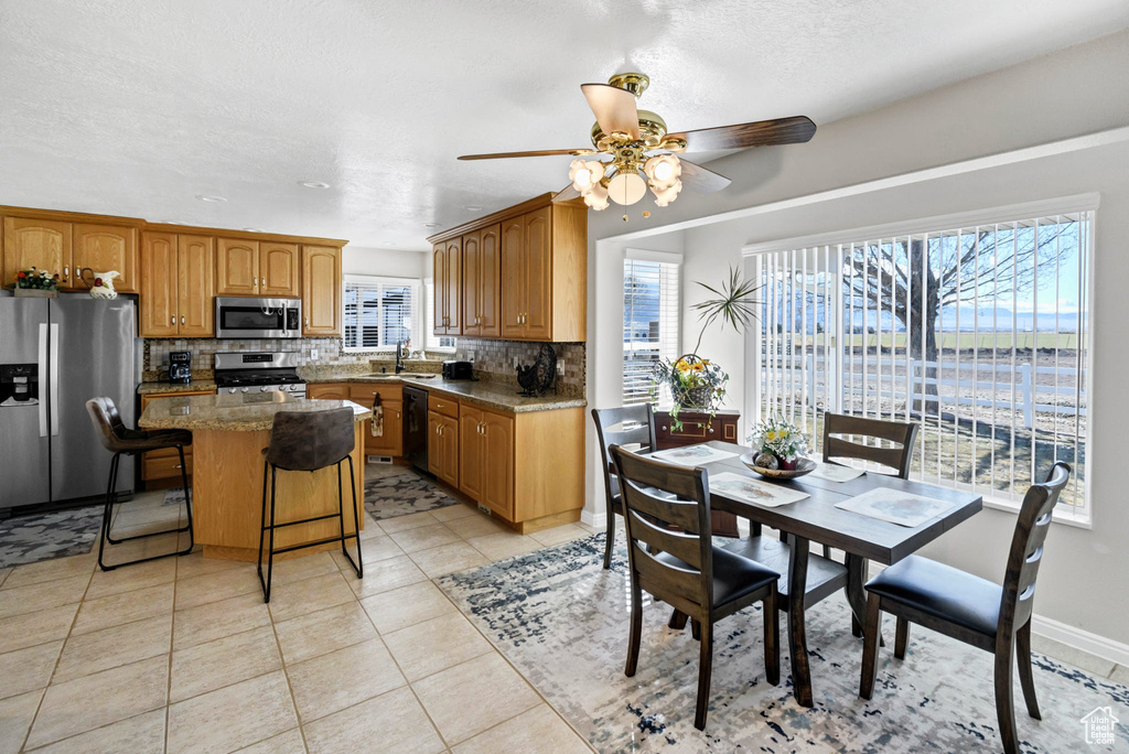 Kitchen featuring appliances with stainless steel finishes, backsplash, a center island, a kitchen bar, and light tile patterned flooring
