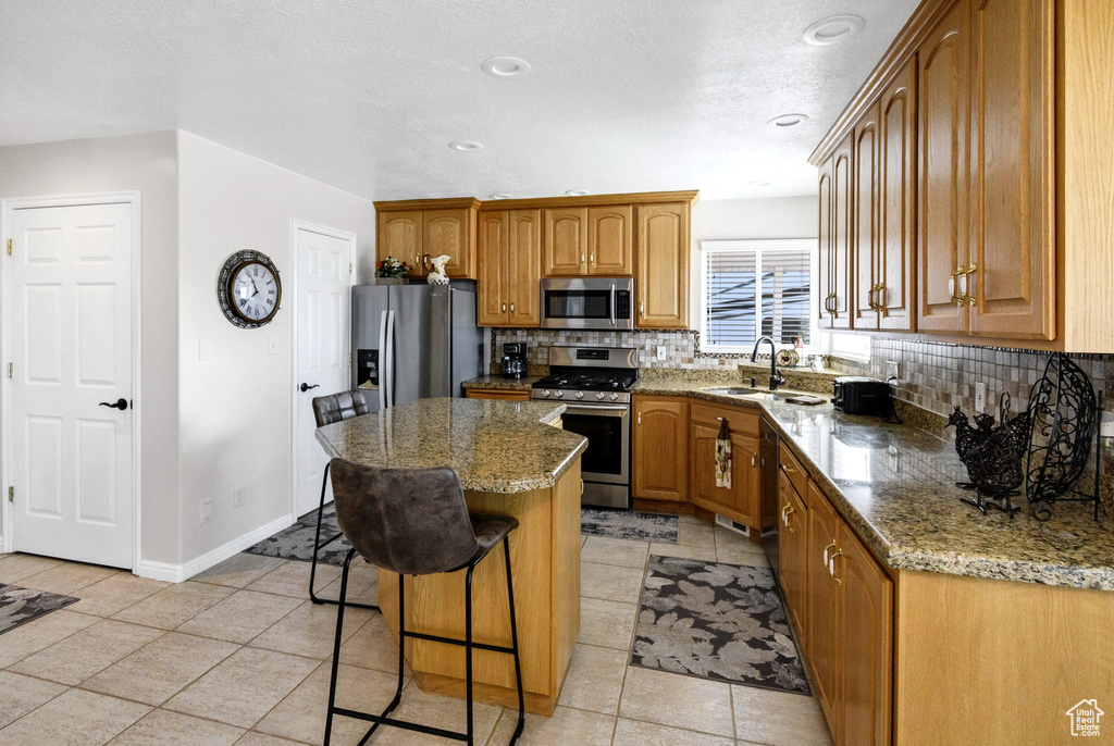 Kitchen with a kitchen island, light stone countertops, appliances with stainless steel finishes, and tasteful backsplash