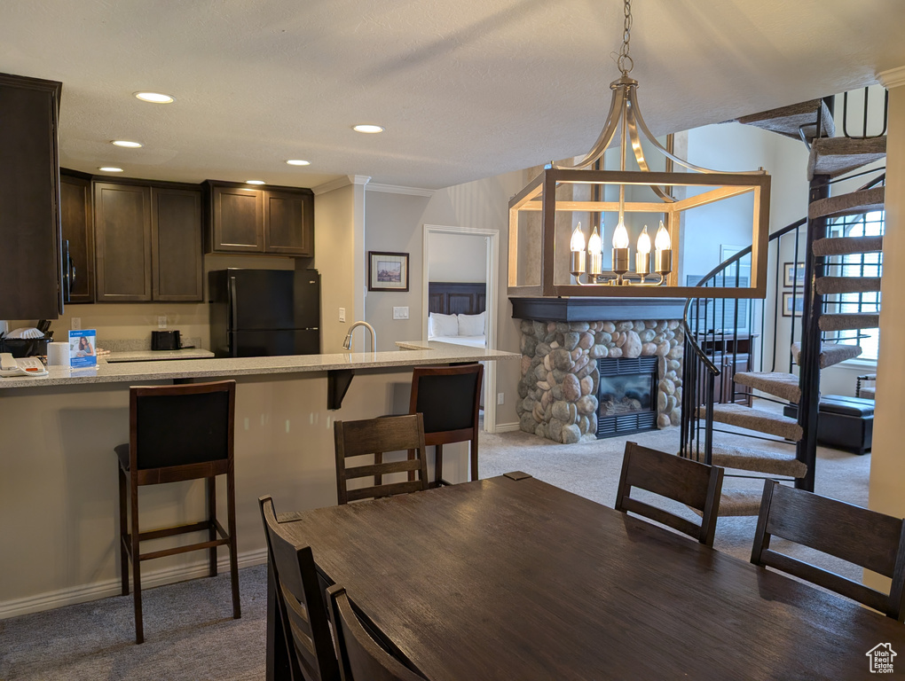 Dining area featuring a stone fireplace, a chandelier, and dark colored carpet