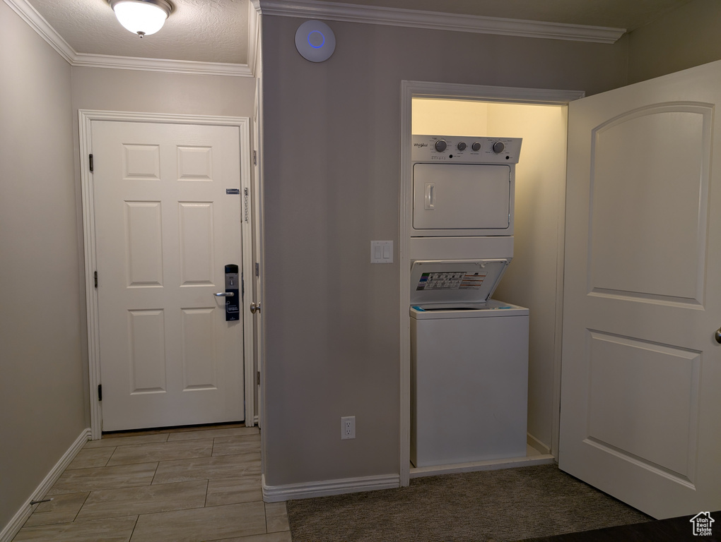Clothes washing area featuring stacked washing maching and dryer, a textured ceiling, and crown molding