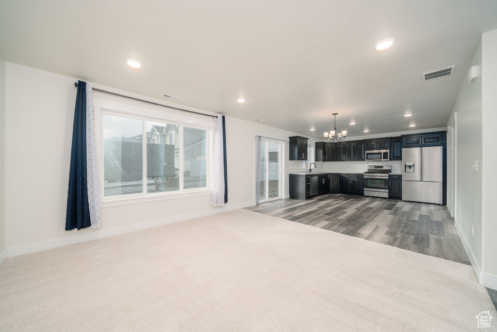 Unfurnished living room with sink, light colored carpet, and a chandelier