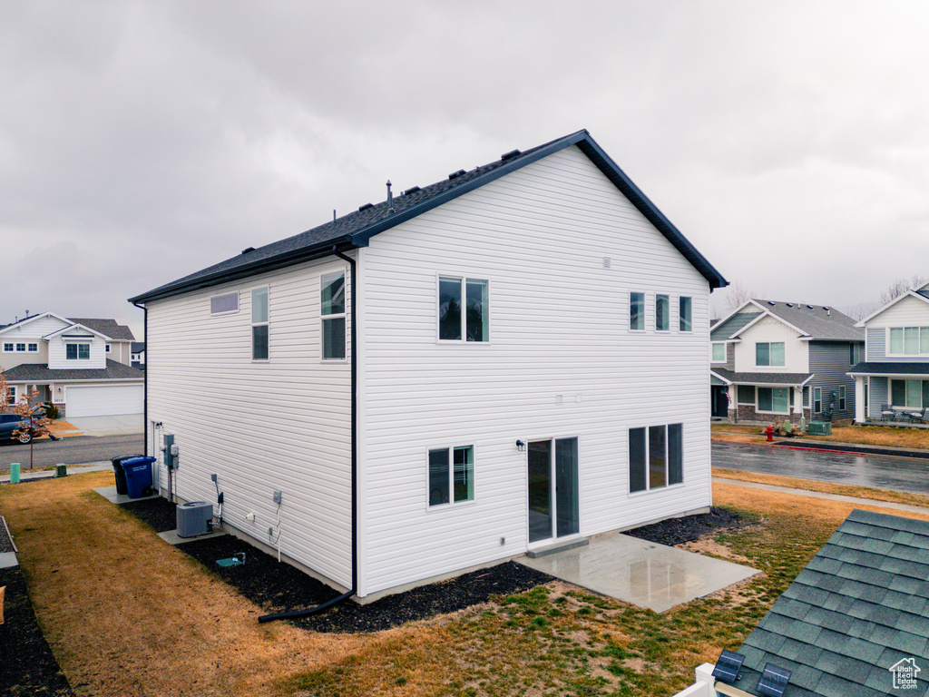 Back of house with cooling unit, a lawn, and a patio