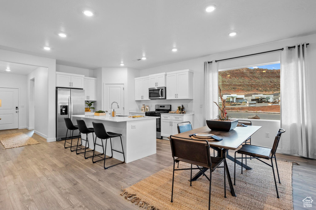 Kitchen featuring light hardwood / wood-style flooring, appliances with stainless steel finishes, white cabinetry, a center island with sink, and a kitchen bar