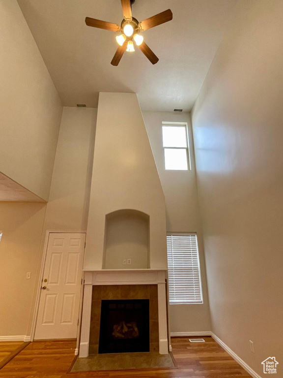 Unfurnished living room featuring a tiled fireplace, hardwood / wood-style floors, ceiling fan, and a high ceiling