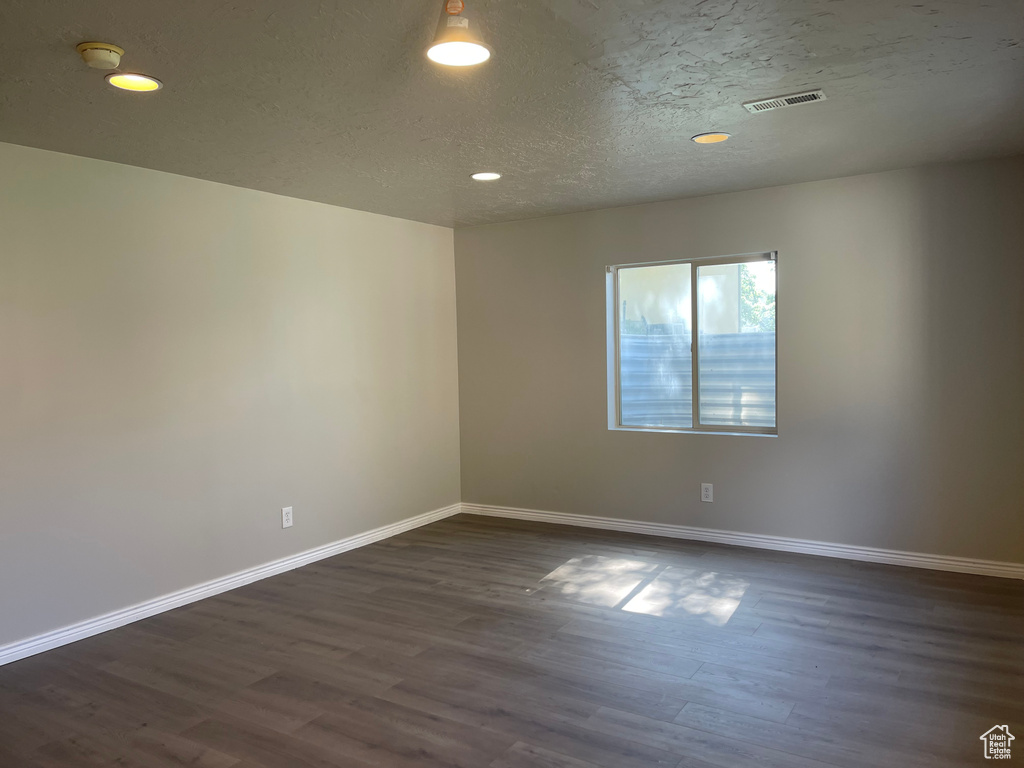 Empty room featuring dark wood-type flooring and a textured ceiling