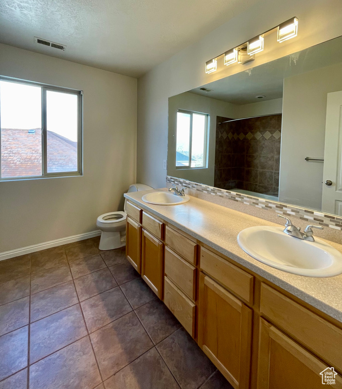 Bathroom with tiled shower, vanity, toilet, and tile patterned flooring