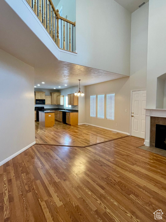 Unfurnished living room with a notable chandelier, hardwood / wood-style flooring, a tile fireplace, and a towering ceiling