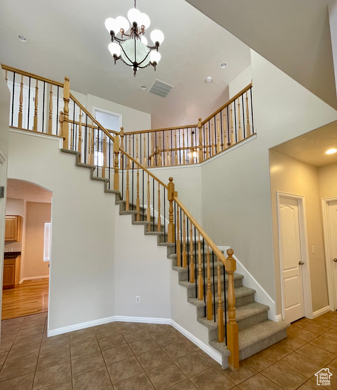 Staircase with a towering ceiling, tile patterned floors, and a chandelier