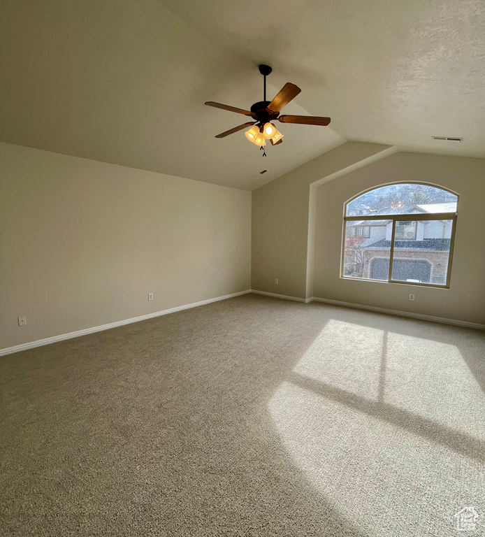 Carpeted spare room featuring ceiling fan and vaulted ceiling