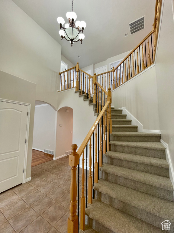 Stairway featuring a towering ceiling, tile patterned floors, and a chandelier
