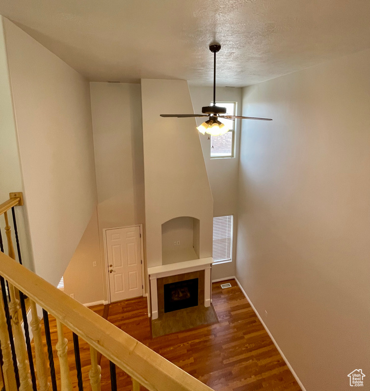 Unfurnished living room featuring hardwood / wood-style flooring, ceiling fan, a fireplace, and a textured ceiling