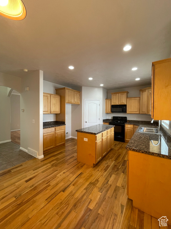 Kitchen featuring sink, dark stone countertops, hardwood / wood-style floors, black appliances, and a kitchen island