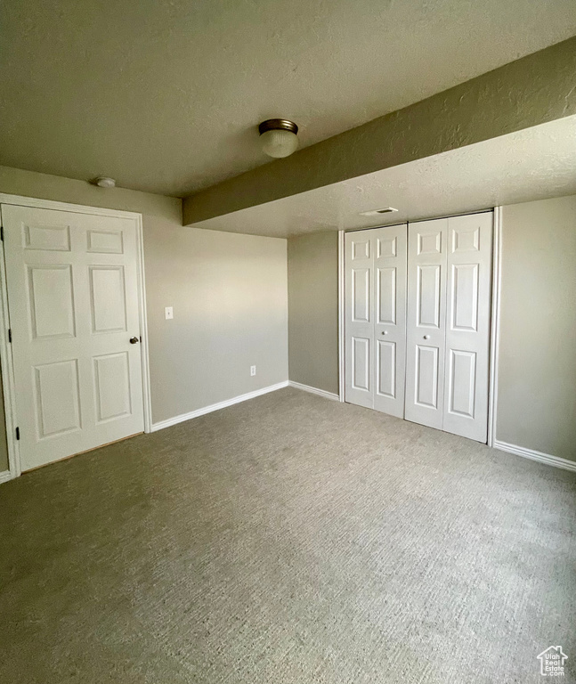 Unfurnished bedroom featuring a closet, a textured ceiling, and dark colored carpet