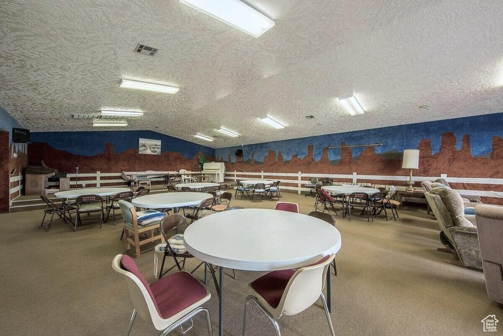 Dining room featuring visible vents, carpet, a textured ceiling, and lofted ceiling