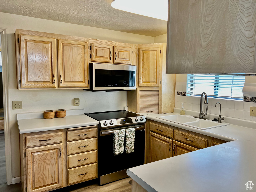Kitchen with decorative backsplash, light brown cabinetry, a sink, light countertops, and stainless steel appliances