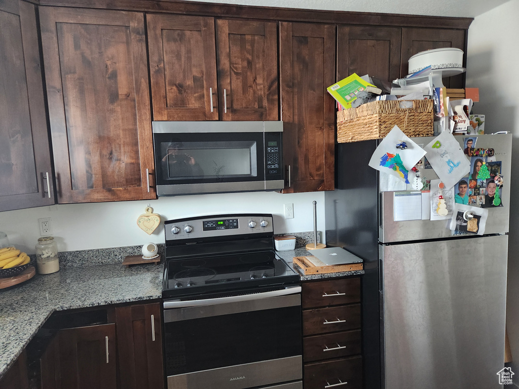 Kitchen featuring dark brown cabinetry, appliances with stainless steel finishes, and light stone countertops