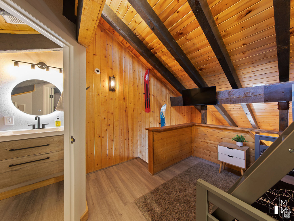 Additional living space with light hardwood / wood-style flooring, wooden ceiling, beamed ceiling, and wood walls