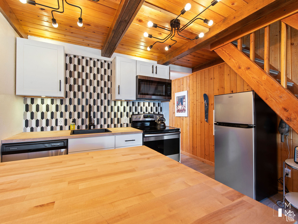 Kitchen with sink, butcher block countertops, white cabinetry, wood ceiling, and appliances with stainless steel finishes