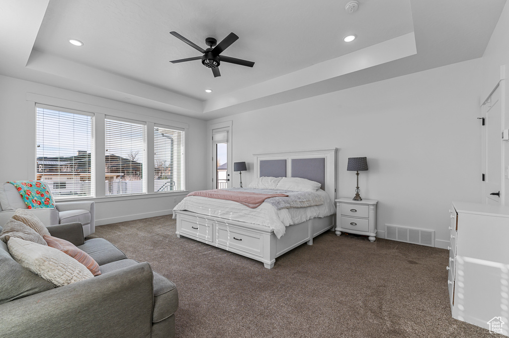 Bedroom with a tray ceiling, ceiling fan, and dark colored carpet