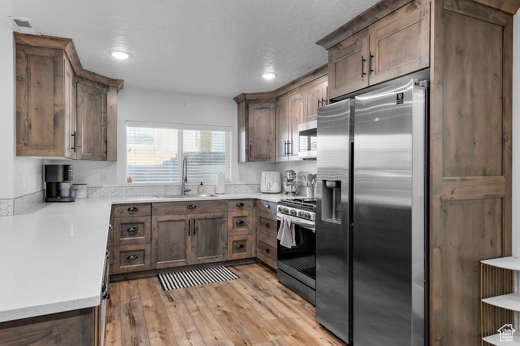 Kitchen featuring sink, dark brown cabinets, light hardwood / wood-style flooring, a textured ceiling, and appliances with stainless steel finishes