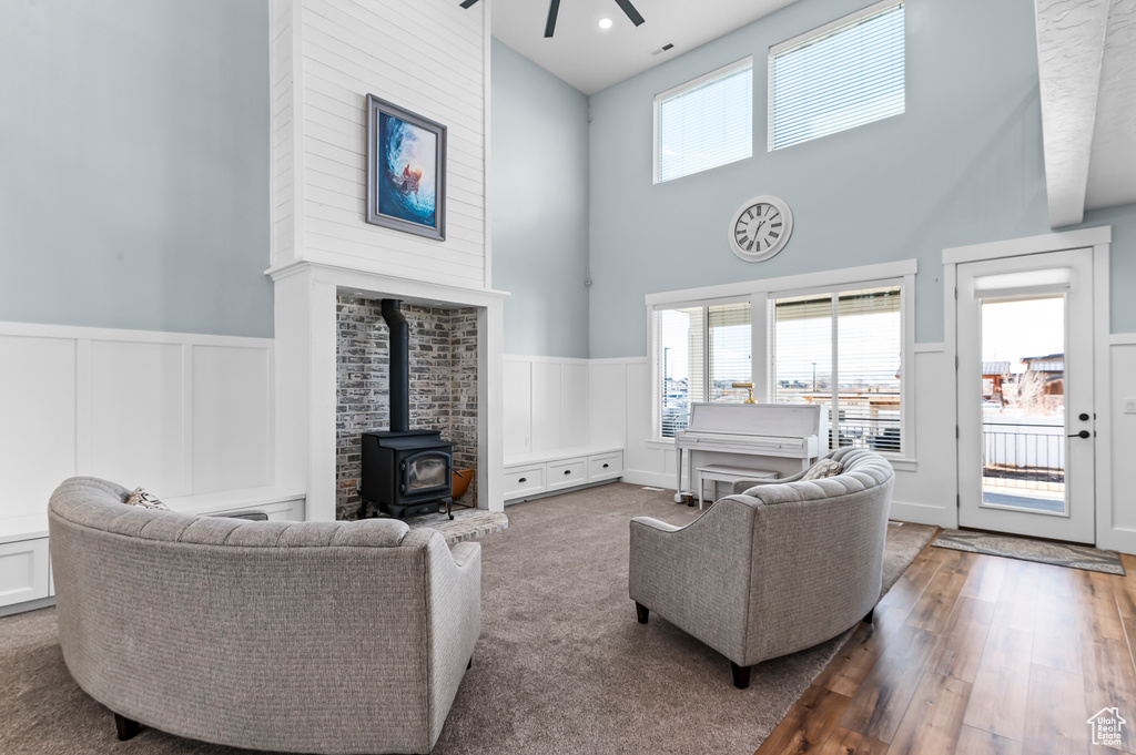 Living room featuring hardwood / wood-style flooring, a wood stove, ceiling fan, and a towering ceiling