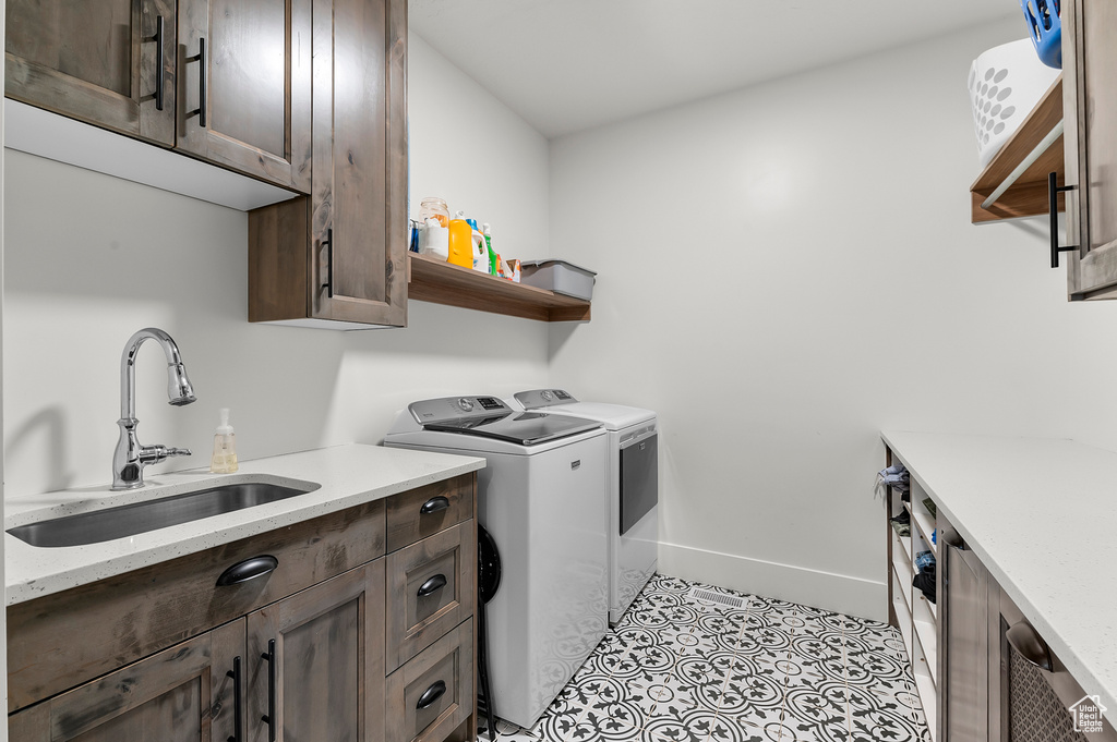 Clothes washing area with light tile patterned flooring, cabinets, sink, and washing machine and dryer