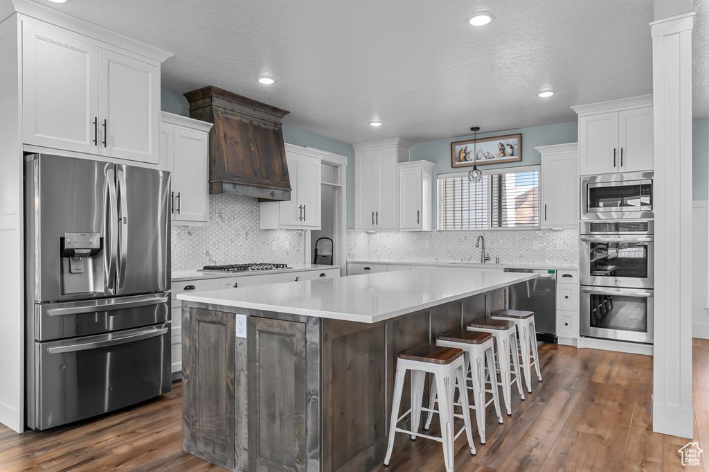 Kitchen featuring a kitchen island, appliances with stainless steel finishes, dark hardwood / wood-style floors, white cabinets, and a kitchen breakfast bar