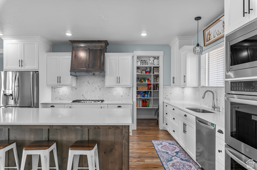 Kitchen featuring premium range hood, sink, appliances with stainless steel finishes, a kitchen breakfast bar, and white cabinets