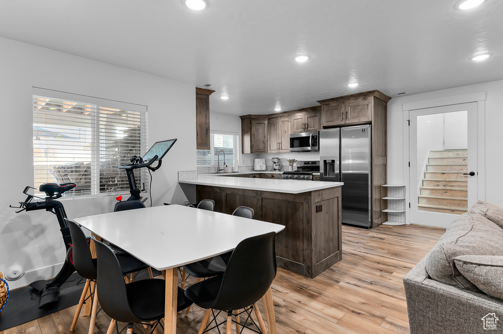 Kitchen featuring light hardwood / wood-style flooring, a kitchen breakfast bar, kitchen peninsula, and appliances with stainless steel finishes