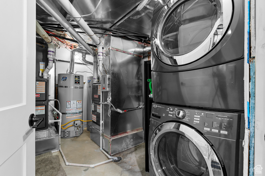 Washroom featuring strapped water heater, stacked washing maching and dryer, and heating unit