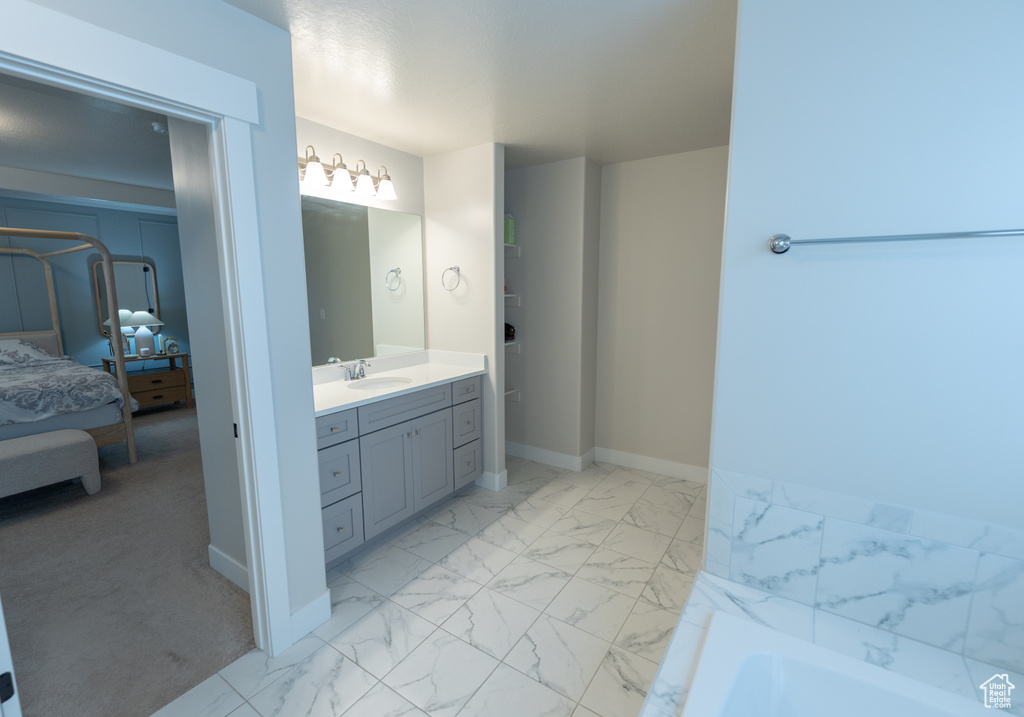 Ensuite bathroom with marble finish flooring, vanity, a bathtub, and baseboards