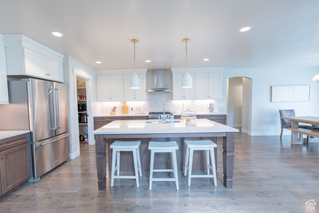 Kitchen with freestanding refrigerator, wall chimney exhaust hood, arched walkways, a sink, and a breakfast bar area