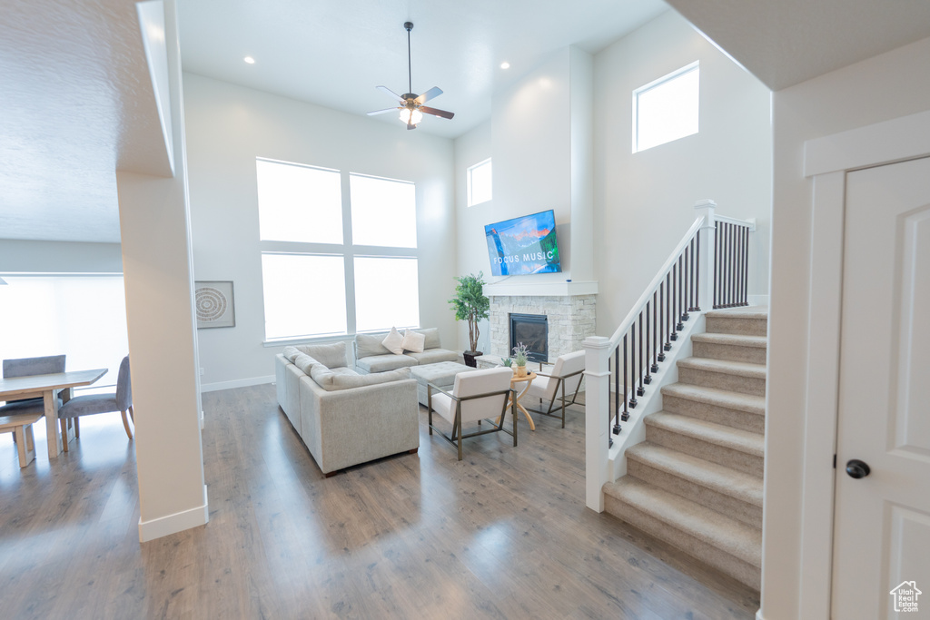 Living area with ceiling fan, a high ceiling, a fireplace, stairs, and wood finished floors