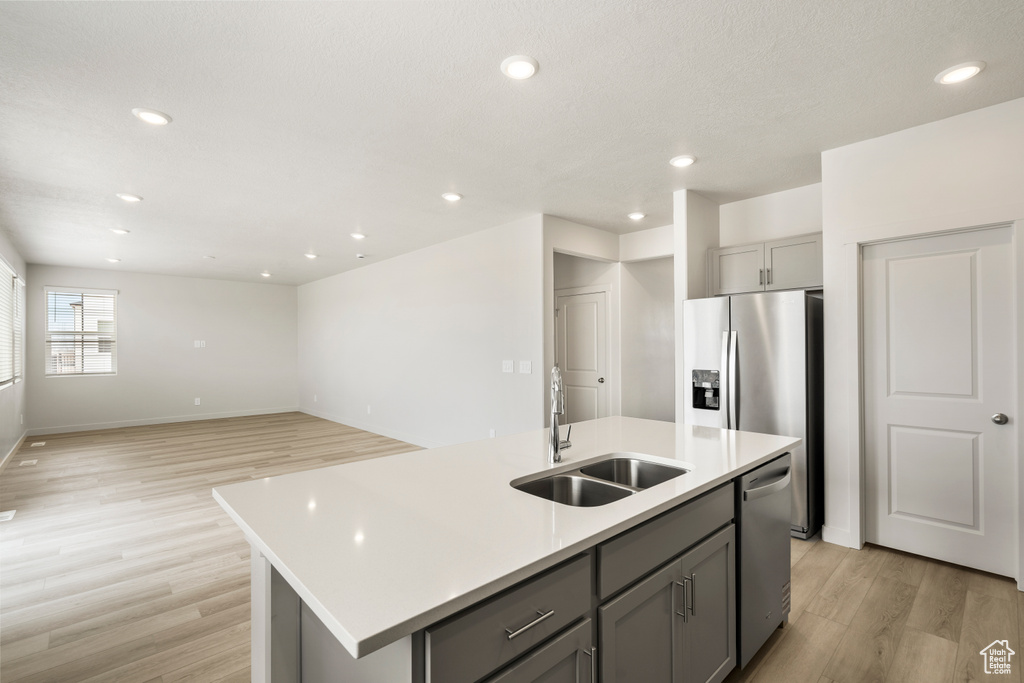Kitchen featuring a sink, gray cabinets, stainless steel appliances, light wood-type flooring, and an island with sink