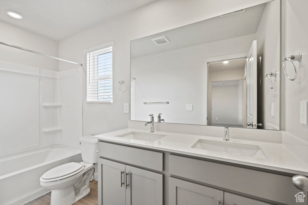 Bathroom featuring toilet, wood finished floors, double vanity, bathtub / shower combination, and recessed lighting