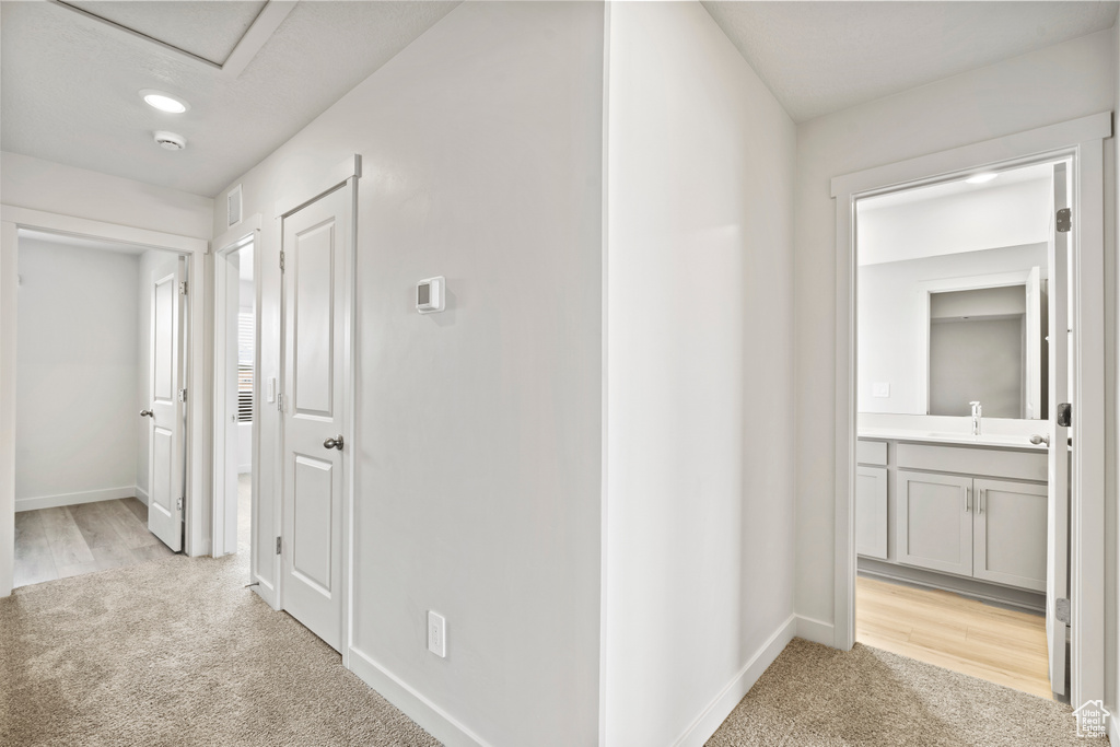 Hall featuring light colored carpet, a sink, and baseboards
