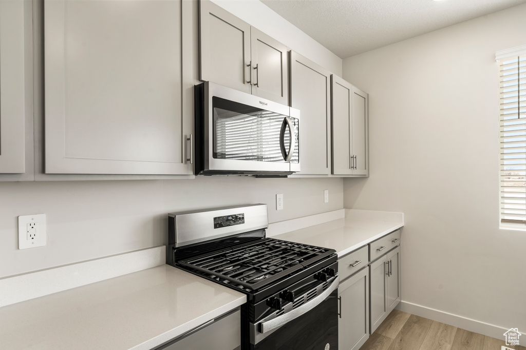 Kitchen with stainless steel appliances, gray cabinets, light wood-style floors, light countertops, and baseboards