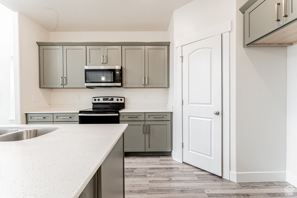 Kitchen with light wood-style flooring, black electric range oven, stainless steel microwave, and gray cabinets