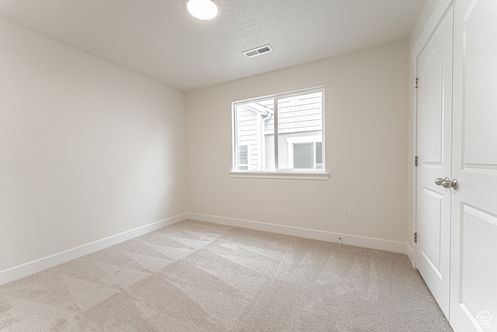 Unfurnished bedroom with light colored carpet, baseboards, a textured ceiling, visible vents, and a closet
