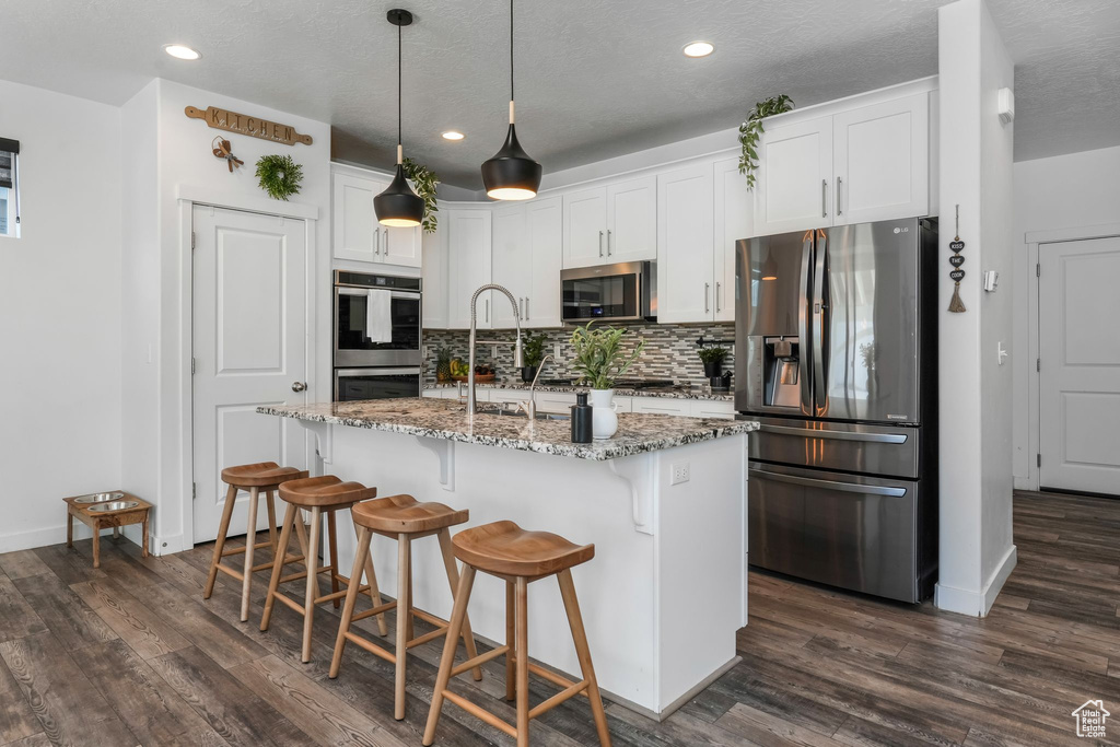 Kitchen with appliances with stainless steel finishes, baseboards, backsplash, recessed lighting, and light stone counters
