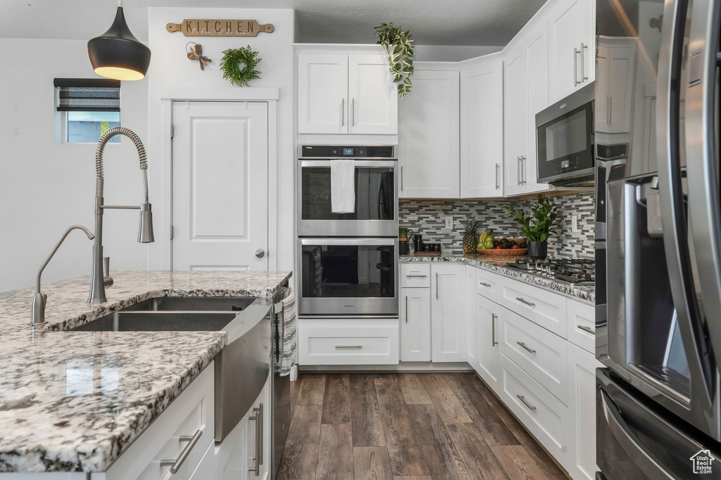 Kitchen featuring stainless steel appliances, a sink, white cabinets, decorative backsplash, and dark wood finished floors