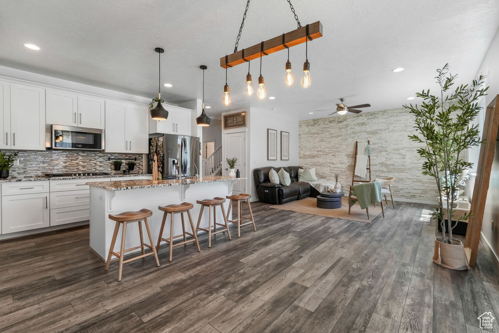 Kitchen with stainless steel appliances, a ceiling fan, dark wood-style floors, a breakfast bar, and recessed lighting