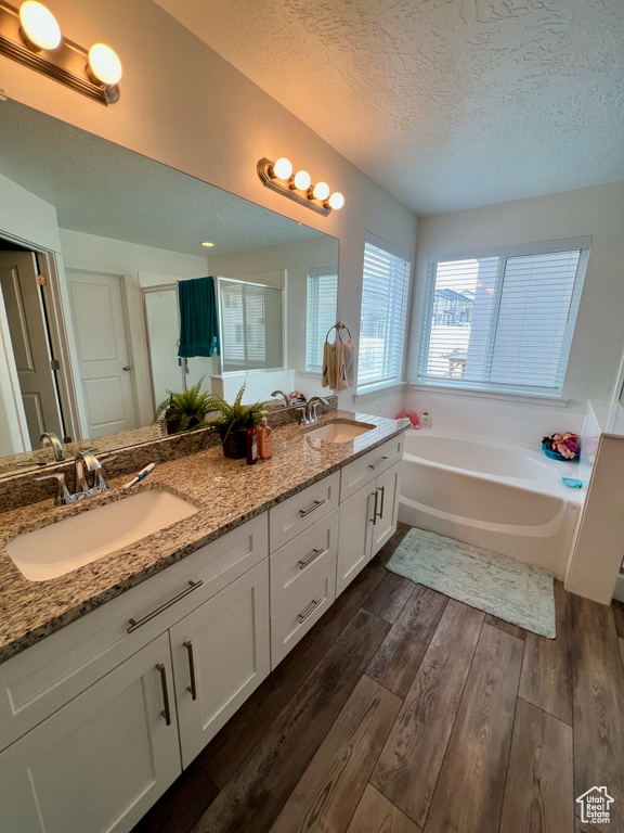 Full bathroom featuring a textured ceiling, a bath, double vanity, wood finished floors, and a stall shower