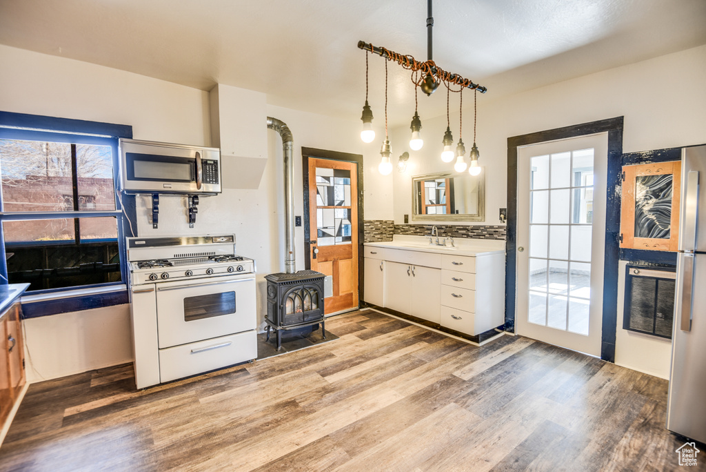 Kitchen with hanging light fixtures, appliances with stainless steel finishes, white cabinets, light hardwood / wood-style floors, and backsplash