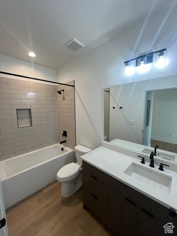 Full bathroom with vanity, hardwood / wood-style flooring, toilet, and tiled shower / bath combo