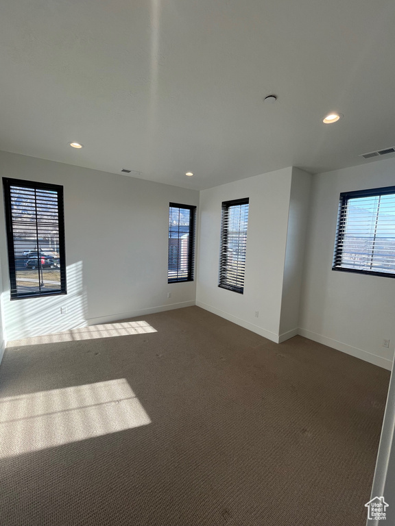 Unfurnished room featuring plenty of natural light and dark carpet