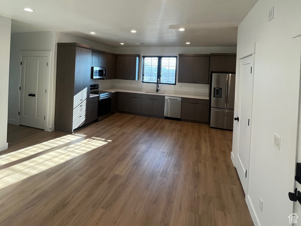 Kitchen with appliances with stainless steel finishes, dark hardwood / wood-style flooring, sink, and dark brown cabinets