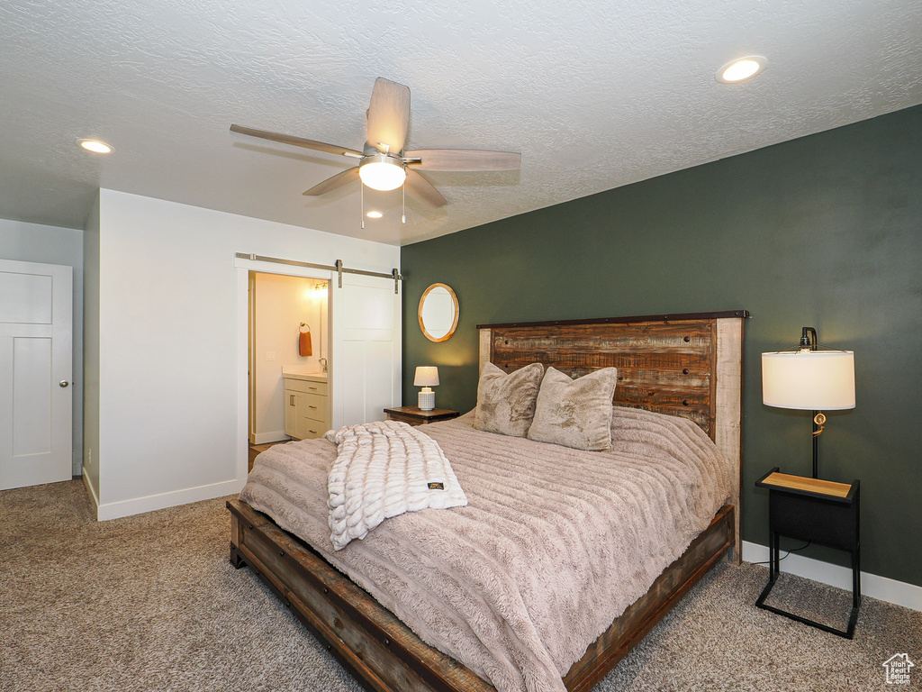 Carpeted bedroom featuring ceiling fan, a barn door, a textured ceiling, and ensuite bath